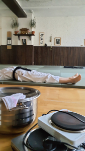 Ein leerer Topf und Herdplatten stehen vor einer liegenden Person im Aikidodojo
